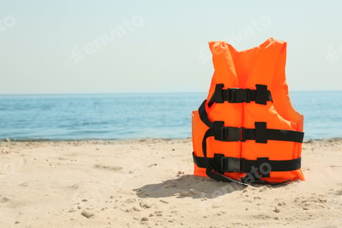 Preview: Orange life jacket on sandy beach near sea. Emergency rescue equipment