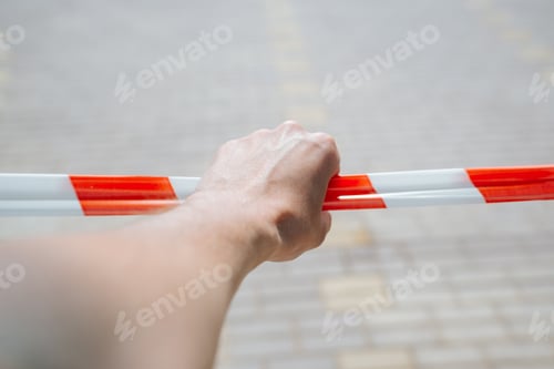 Preview: Close-up of caucasian male hand holding striped red and white tape fencing dangerous area outdoors