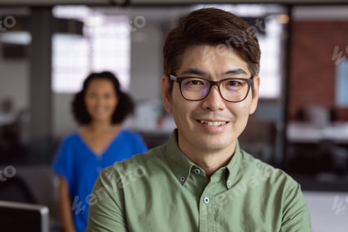 Preview: Portrait of smiling asian businessman standing in office with female colleague in background