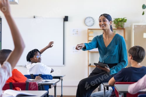 Preview: In school, Indian female teacher holding tablet and engaging with students raising hands