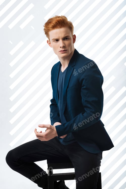 Preview: Very Stylish. Charming Pretty Guy Sitting On Chair And Touching Jacket