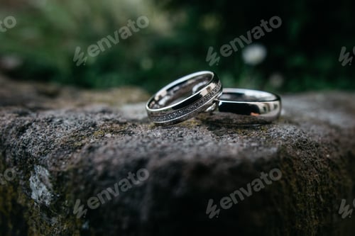 Preview: Closeup of wedding silver rings on the stone outdoors blurred background