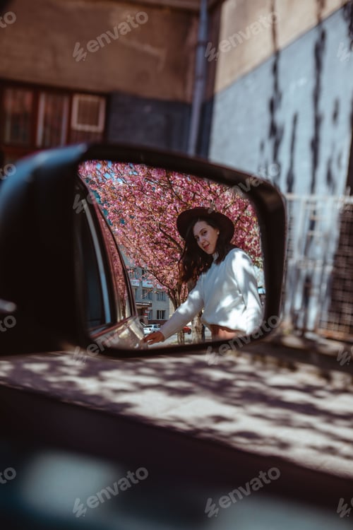 Preview: smiling woman reflection in car rear mirror blooming sakura tree on background