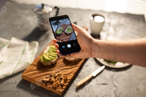 Preview: Hands take pictures on smartphone of two beautiful healthy sour cream and avocado sandwiches lying