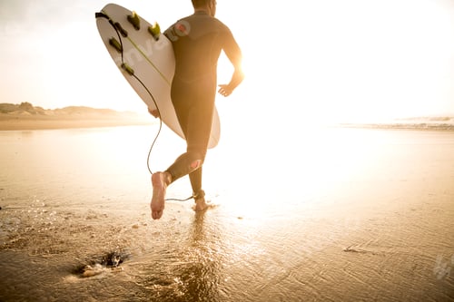 Surfer Running Towards Ocean with Surfboard at Sunset