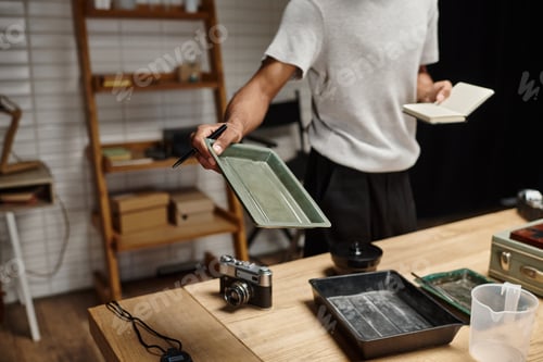 Preview: young african american photographer expertly handles film tray in a modern analog darkroom