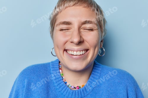 Preview: Close up shot of happy short haired woman keeps eyes closed smiles toothily expresses positive