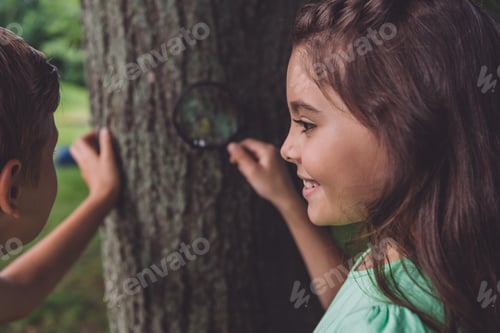 Preview: selective focus of happy kid holding magnifier while standing near tree trunk with friend