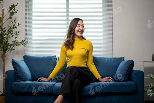 Preview: Young asian woman sitting on couch smiling looking away from camera