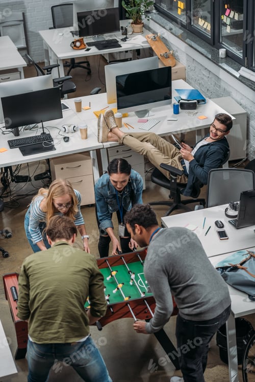 Preview: multicultural people playing in table soccer at modern office