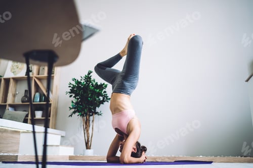 Preview: Sportive Caucasian fitness girl training on caremat standing on head and hands during workout