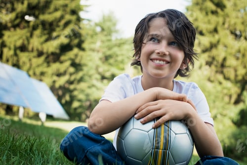 Preview: A boy holding a football, sitting on the grass. Solar panels.