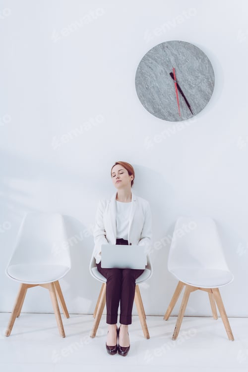 Preview: exhausted employee with laptop sleeping on chair near clock
