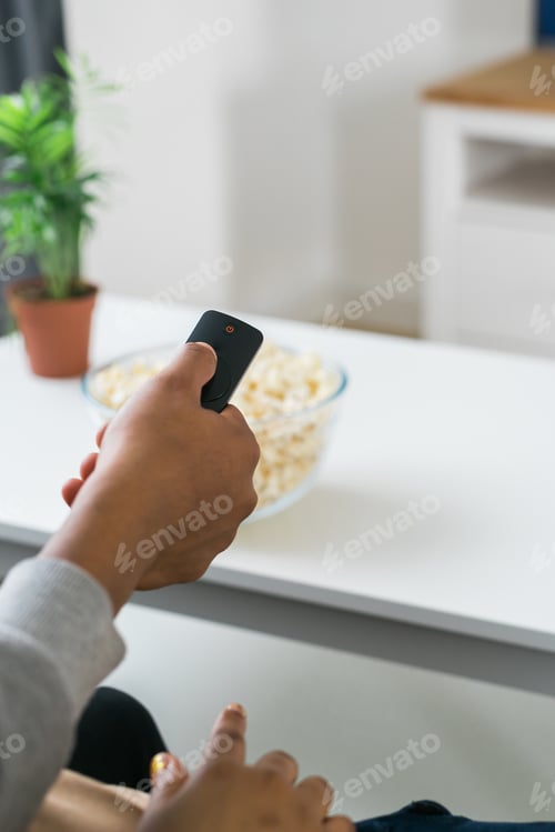 Preview: African american woman sits on a gray sofa, enjoying a bowl of popcorn while watching a movie or