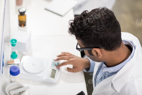 Preview: High angle view of young scientist working with electronic scales in research laboratory