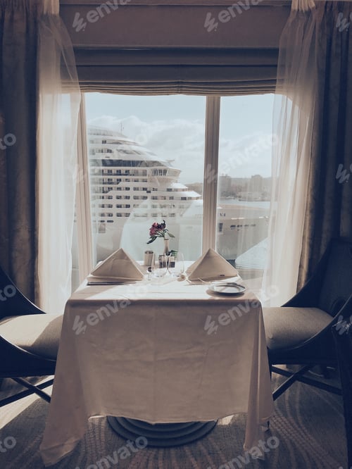 Preview: Dining table in a cruise ship is beautifully set next to a window with another cruise ship nearby.