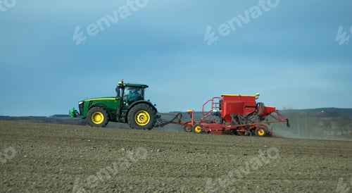 Preview: Modern green tractor pulling a red seed drill in the back on a farm in the Czech Republic