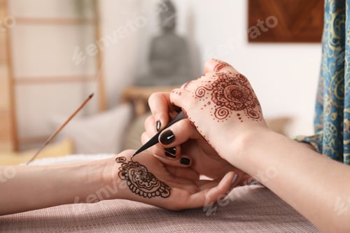 Preview: Professional mehndi master making henna tattoo indoors, closeup