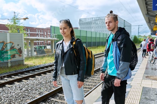 Preview: Students teenage guy and girl with backpacks waiting for commuter train on railway platform