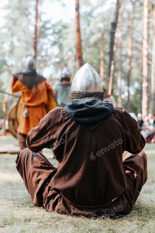 Preview: Medieval soldier in a helmet and ancient clothes sitting on the grass in the forest
