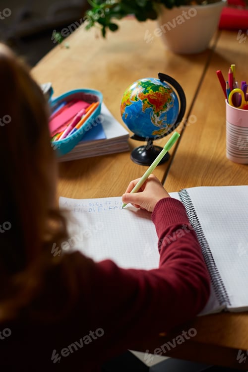 Preview: Focused schoolgirl sit at desk doing homework handwriting, homeschooling.
