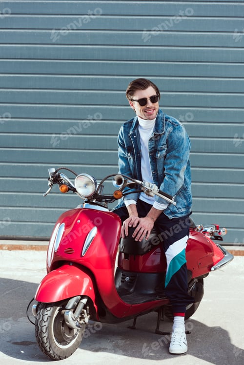 Preview: happy young man on vintage red scooter looking away