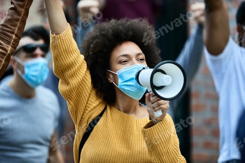 Preview: Black woman with protective face mask shouting through megaphone on public demonstrations.