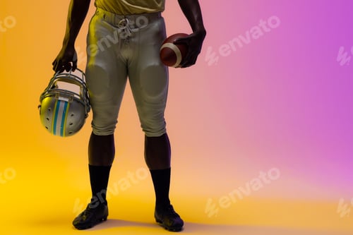 Preview: Midsection of african american male american football player with neon purple and yellow lighting