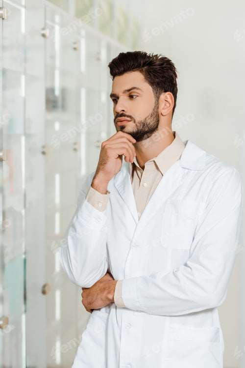 Preview: Thoughtful pharmacist looking at showcase in drugstore