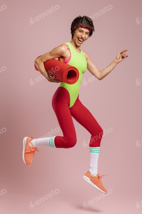 Preview: Happy fit woman in retro styled sports clothing jumping against yellow background
