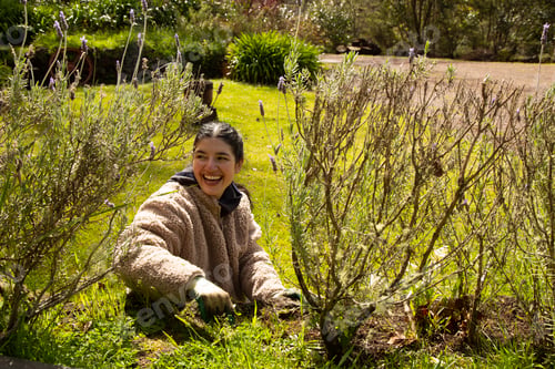Preview: Woman laughing while gardening on a sunny day, surrounded by green plants and flowers