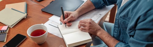 Preview: Close up of man hands making notes in notepad while sitting on his workplace