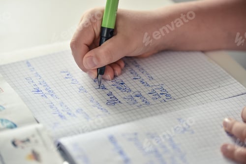 Preview: High angle shot of a female child doing her homework with a blue pen
