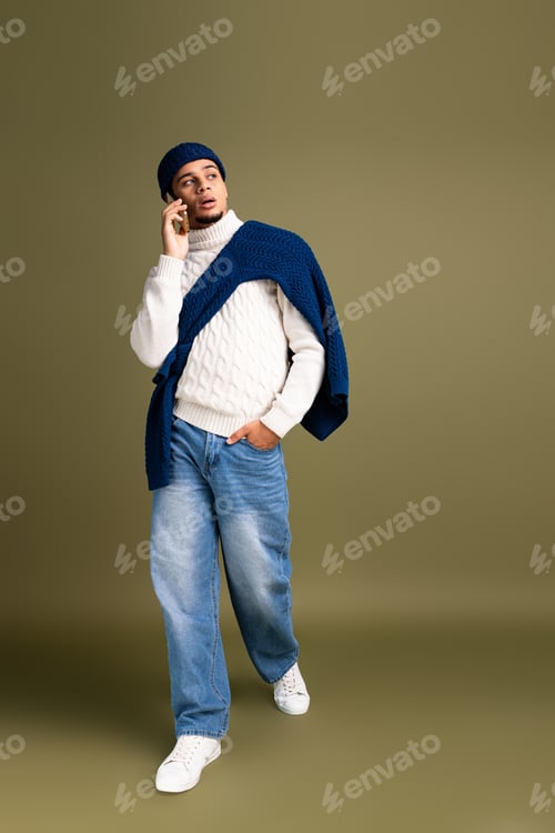 Preview: Handsome young man walking and talking on phone while showcasing trendy winter fashion