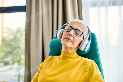 Preview: Senior woman sleeping in armchair with headphones on