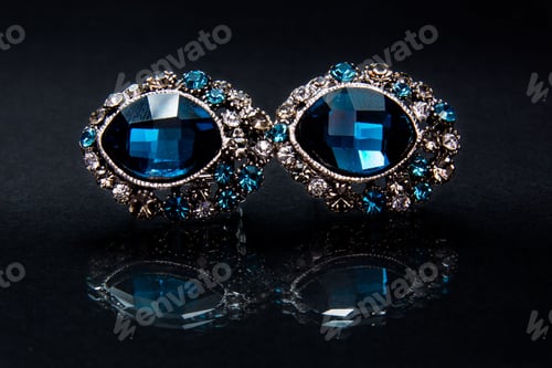 Preview: Pair of large, sparkling blue diamond earrings gleaming brightly against a black surface