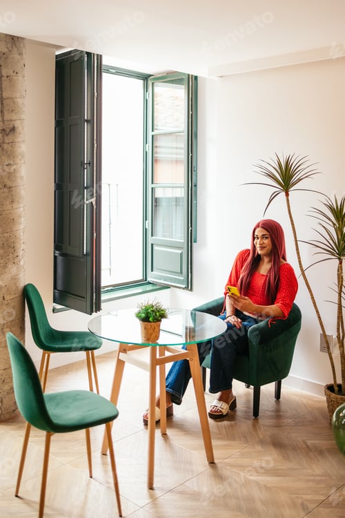 Preview: Transgender influencer relaxing and using smartphone in stylish apartment