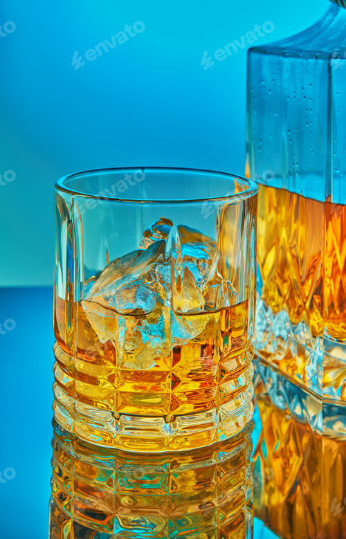 Preview: A glass and square crystal decanter with scotch whiskey or brandy in the background