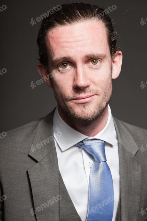 Preview: Young Man Brown Long Hair With Expressive Face Wearing Grey Suit And Blue Tie. Isolated On Grey