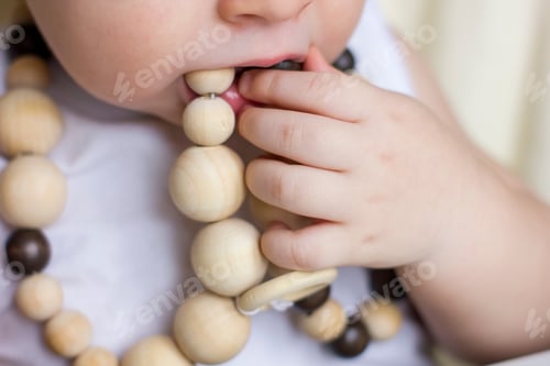 Preview: Closeup baby gnawing modern wooden eco friendly teether.