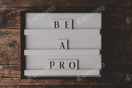 Preview: White sign with writing "Be a pro" on it on a wooden brown background