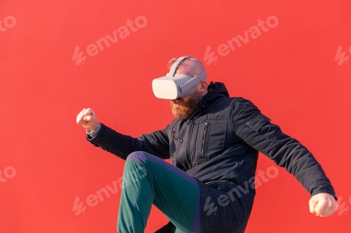 Preview: European man playing fight with virtual reality glasses on red wall background