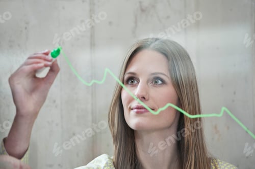 Preview: Germany, North Rhine Westphalia, Cologne, Businesswoman drawing graph on glass, looking away