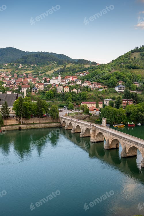 Preview: An old stone bridge with arches spans the tranquil Drina River, surrounded by green hills
