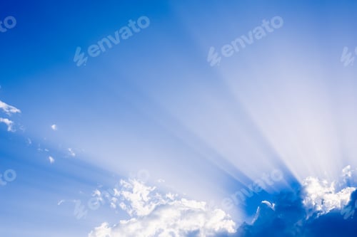 Preview: Sunbeams rising from a large cloud in intense blue sky on a summer afternoon