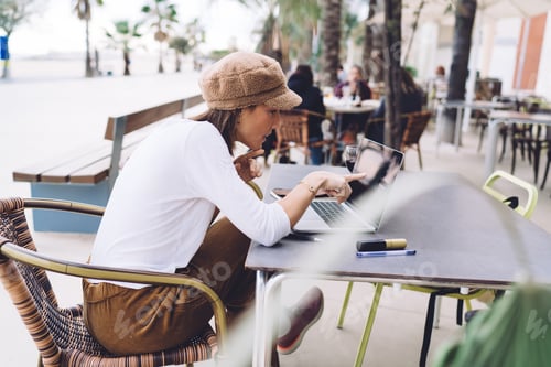 Preview: Positive caucasian female reading information on laptop computer checking mail on cafe terrace