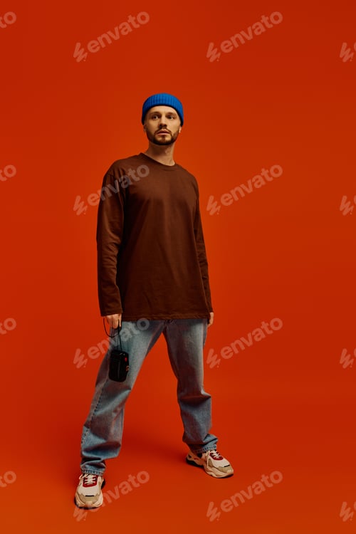 Preview: Handsome young man dressed casually stands confidently against a vibrant orange backdrop