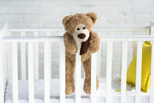 Preview: close up view of teddy bear hanging on white wooden baby crib in room