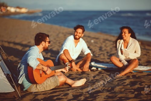 Preview: Happy friends sitting on the beach singing and playing guitar