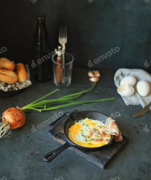 Preview: Scrambled eggs with bacon in a frying pan on the table, beer and other ingredients for a substantial